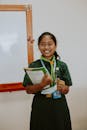 Cheerful student in uniform holding a notebook, standing in a classroom.