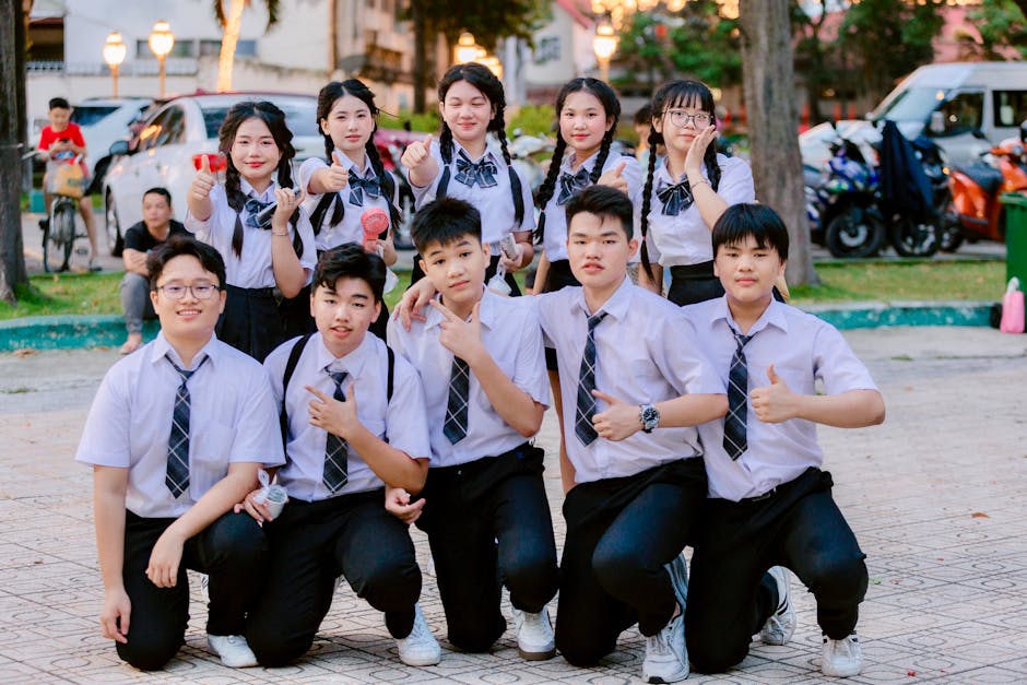 Cheerful group of students in uniform posing with thumbs up outdoors.