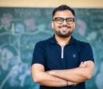 Smiling educator standing confidently in front of a chalkboard, exuding positivity and professionalism.