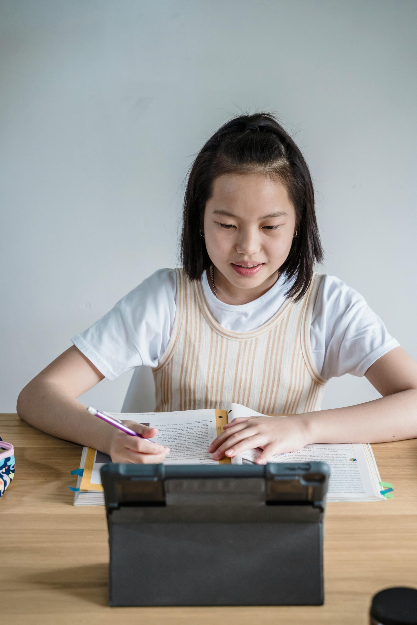 An Asian girl focusing on online classes, studying at a table indoors.