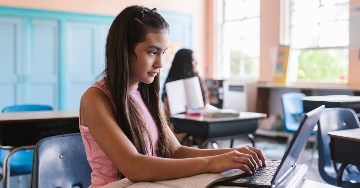 Young girl engaged with a laptop in a classroom environment, illustrating focused learning.